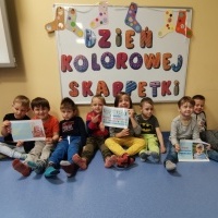 Grupa dzieci siedzi na podłodze. W tle napis Dzień kolorowej skarpetki.