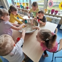 Dzieci siedzą przy stole i nabierają ryż z dużej miski.