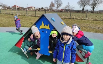 Grupa dzieci na placu zabaw w domku pozuje do zdjęcia.