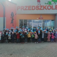 Światowy Dzień Świadomości Autyzmu zdjęcie grupowe wszystkich grup młodszych przed budynkiem przedszkola, dzieci trzymają w rękach niebieskie chorągiewki.