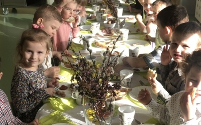 Grupa dzieci siedzi przy wielkanocnym stole. Na stole śniadanie wielkanocne i dekoracje.