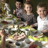 Grupa dzieci siedzi przy wielkanocnym stole. Na stole śniadanie wielkanocne i dekoracje.