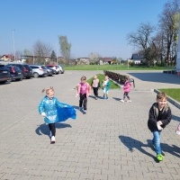 Grupa dzieci sprząta śmieci na terenie przedszkola.