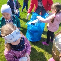Grupa dzieci wrzuca śmieci do dużego niebieskiego worka.