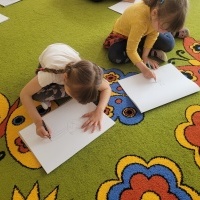 Dwie dziewczynki rysują kota na dużym arkuszu papieru 