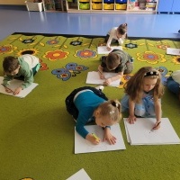 Dzieci siedzą na dywanie. Rysują zwierzątka na dużym arkuszu papieru
