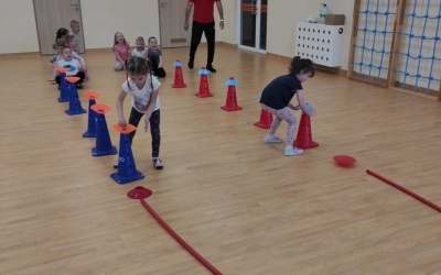  Dzieci wykonują ćwiczenia wg instrukcji trenera na sali gimnastycznej. 