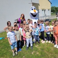 Dzieci stoją na podwórku przy dużej maskotce Olafa. 