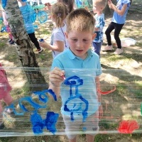 Chłopiec w niebieskiej bluzce maluje farbami na folii