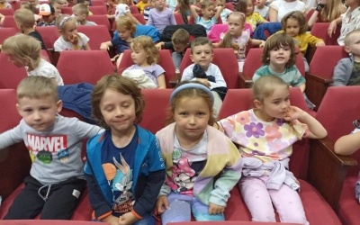 Dzieci siedzą w sali kinowej na przedstawieniu Pchła Szachrajka i Piękna i Bestia.