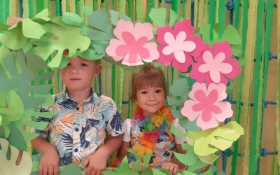 Chłopczyk i dziewczynka pozujący do zdjęcia w scenerii hawajskiej , wokół kolorowych kwiatów. 