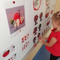 Dziewczynka rozwiązuje zadanie matematyczne o jabłkach. W tle tablica. 