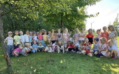 Grupa Żabki i Pszczółki pozuje do zdjęcia w ogrodzie warzywnym, dzieci ustawione są w dwóch rzędach, jedna dziewczynka trzyma w rękach bukiet bazylii, chłopiec trzyma ogórka.