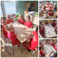 Grupa dzieci ubrana na czerwono siedzi przy stolikach i zjada jabłka.