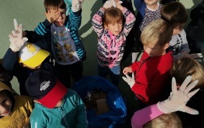 Dzieci podnoszące rączki do góry i demonstrujące nazbierane śmieci.