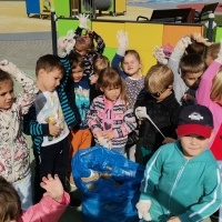 Dzieci stojące dookoła nazbieranych śmieci na boisku przedszkolnym. 