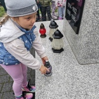 Dziewczynka kładzie znicz przed pomnikiem 