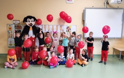 Myszka Miki wraz z dziećmi i balonami pozuje do zdjęcia.
