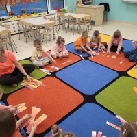 Grupa dzieci siedzi na dywanie. Dzieci układają puzzle z dynią. 