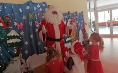 Mikołaj i dzieci stoją w sali. W tle świąteczna dekoracja. 