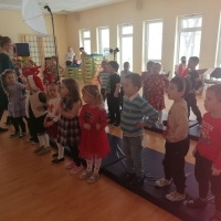 Dzieci stoją w sali gimnastycznej. Śpiewają piosenkę. 
