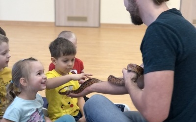 Kilkoro dzieci obserwuje węża, którego trzyma na ręce właściciel prowadzący pokaz.