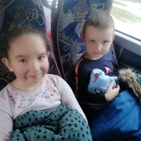 Dwójka dzieci siedzi w autobusie. W tle okno. 