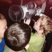 Chłopiec patrzy przez teleskop. W tle inne dzieci.