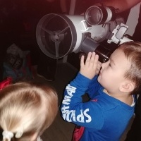 Chłopiec patrzy przez teleskop. W tle inna dziewczynka. 