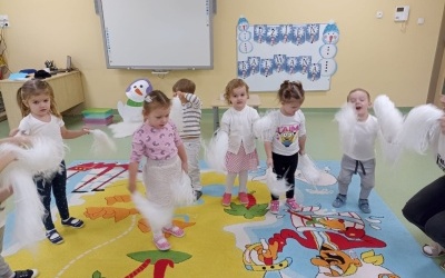 Grupa dzieci tańczy z białymi pomponami. W tle widać bałwanka oraz tablicę z napisem Dzień bałwanka.