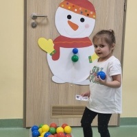 Dziewczynka w białej bluzce przykleja kolorowe piłki na szablonie bałwanka.