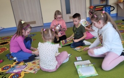 Grupa dzieci siedzi na dywanie i ogląda książki.
