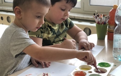Dwóch chłopców siedzi przy stoliku, malują skamieniałości wykonane z masy solnej.