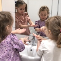 Trzy dziewczynki myją ręce w łazience przedszkolnej.