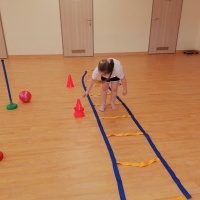 Dzieci ćwiczą na sali gimnastcznej. Dziewczynka pokonuje tor przeszkód. 