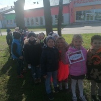 Dzieci w parach stoją przed przedszkolem. Dziewczynka w rękach trzyma napis Biedronki. 