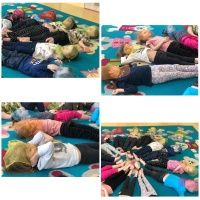Grupa dzieci w ramach Tygodnia Uważności leży na dywanie, na głowach mają kolorowe chustki. Dzieci relaksują się przy muzyce.