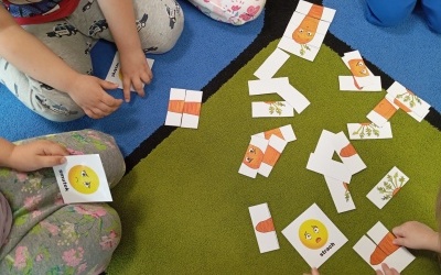Dzieci siedzą na dywanie i odnajdują buźki z emocjami łącząc je z minkami marchewek.