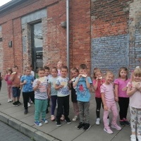 Dzieci stoją przy budynku. Jedzą wafelki. 