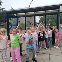 Dzieci czekają na przystanku autobusowym. W tle przystanek. 