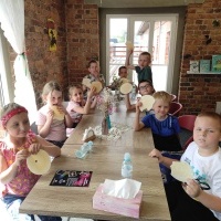 Grupa dzieci siedzą przy stoliku i jedzą wafelki. 