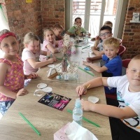 Grupa dzieci siedzi przy stole. Tworzą ze słomek rybki. 