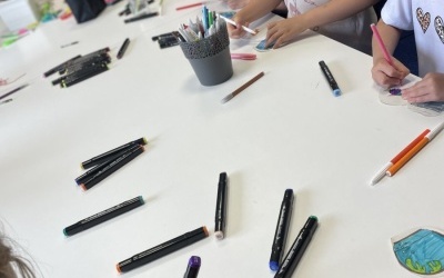 Grupa dzieci siedzi przy stoliku, rysują mazakami.
