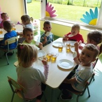 Grupa dzieci siedzi przy stoliku i je lody.  w tle widać inne dzieci.